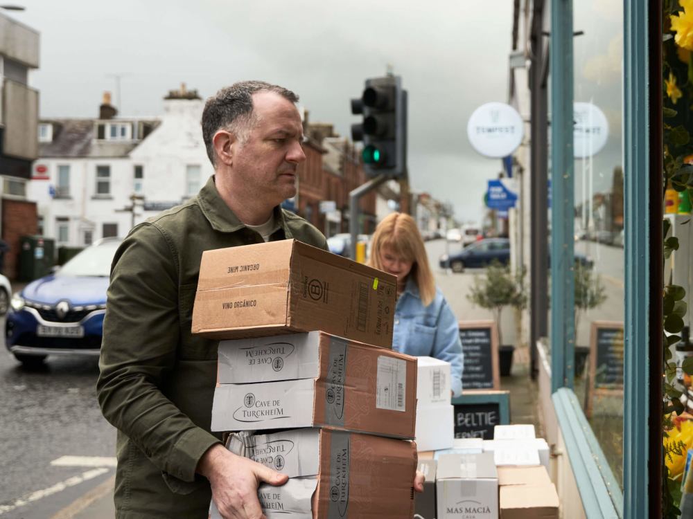 Chris and Lynsey in front of the shop handling a delivery of wine boxes.