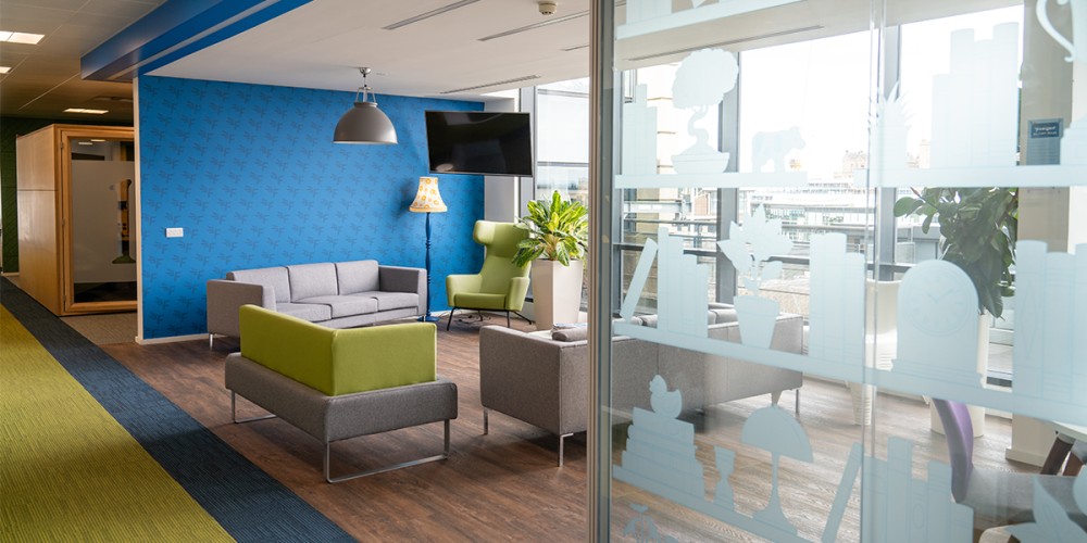 View of the FreeAgent office including a flexible collaboration area with sofas and glass wall. 