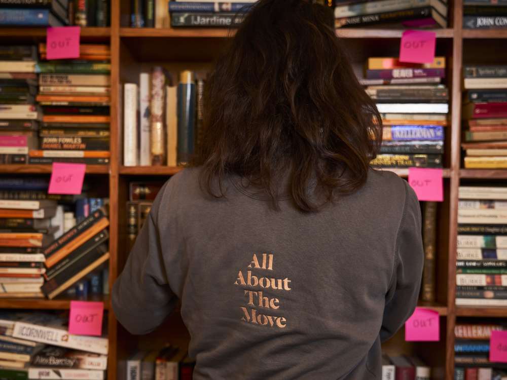 Kath stands in front of a bookcase packed with books and marked with Post It notes.