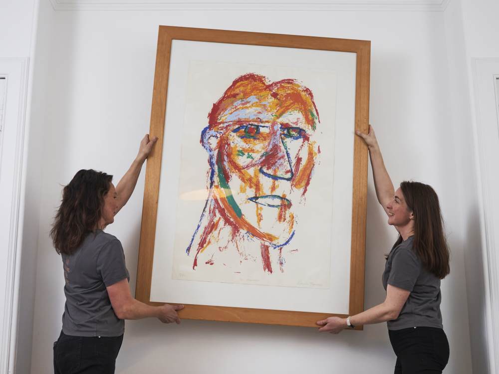 Kath and Zoë removing a large artwork from a wall.