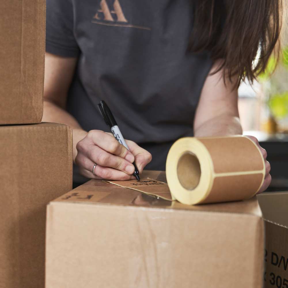 A close-up showing hands writing a sticky label to go on a cardboard box.