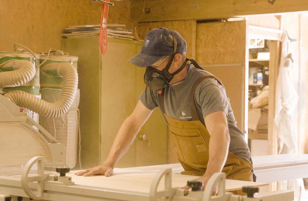 Nathan wears a safety mask as he cuts a large sheet of wood.