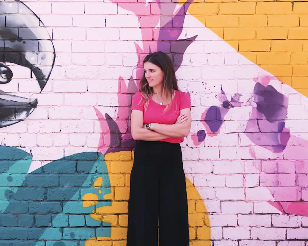 Video thumbnail showing FreeAgent customer, Zoe East, standing against a wall with a colourful mural painted on it.