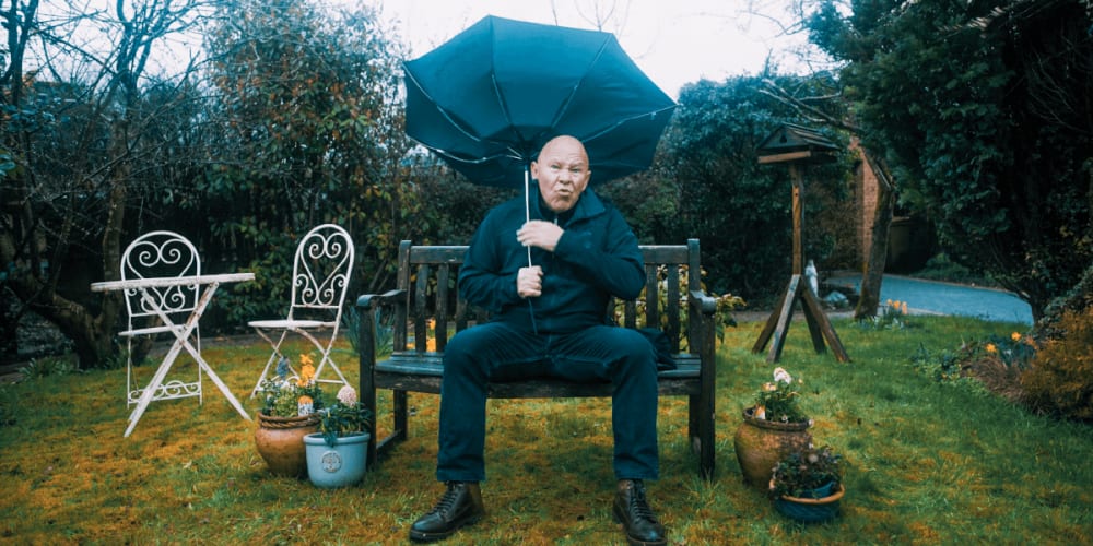 Dom Littlewood sitting on a bench, as his brolly blows inside out.
