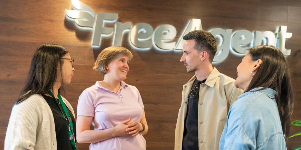 Four people smiling and talking in front of the FreeAgent logo.