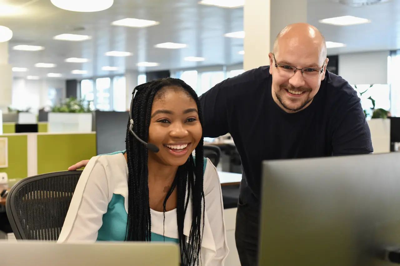 A woman and a man from FreeAgent's Customer Support smiling at their computer screens