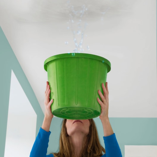 Landlord catching water dripping from ceiling in a green bucket.